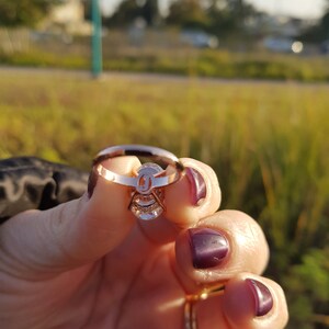 Underside view of an oval moissanite engagement ring held between fingers, showing the open setting beneath the center stone and pavé shank.