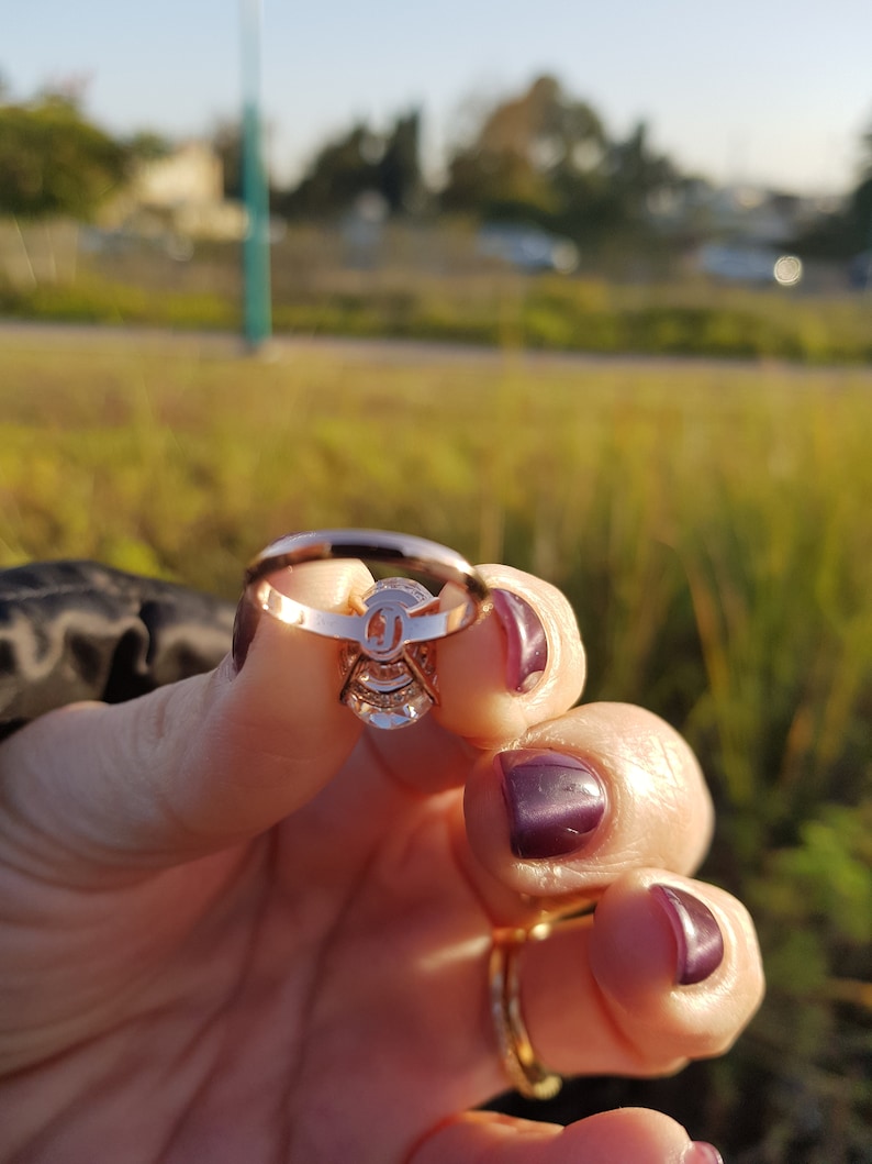 Underside view of an oval moissanite engagement ring held between fingers, showing the open setting beneath the center stone and pavé shank.