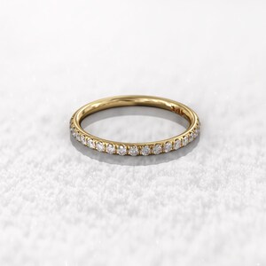May include: A thin gold band with a row of small diamonds set around the entire band.