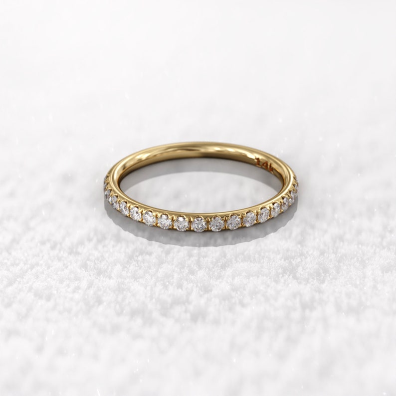 May include: A thin gold band with a row of small diamonds set around the entire band.