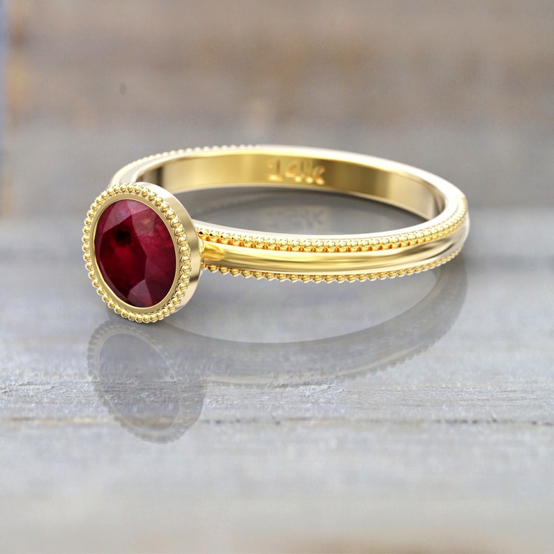 Rear angled view of a yellow gold round ruby engagement ring, showing the inside of the band, smooth bezel setting, and beaded detailing around the stone and band edges.