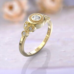 Op de afbeelding: Een gouden ring met een ronde, bezel-gezet diamant omgeven door een parelhalo. De ring heeft een delicaat, bladvormig ontwerp met kleinere diamanten aan elke kant.