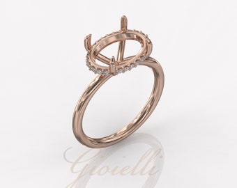 Puede incluir: Anillo de oro rosa con un engaste de halo ovalado, adornado con pequeñas piedras brillantes. El anillo presenta una banda delicada y garras diseñadas para sostener una piedra central. La palabra "Gioielli" es visible.