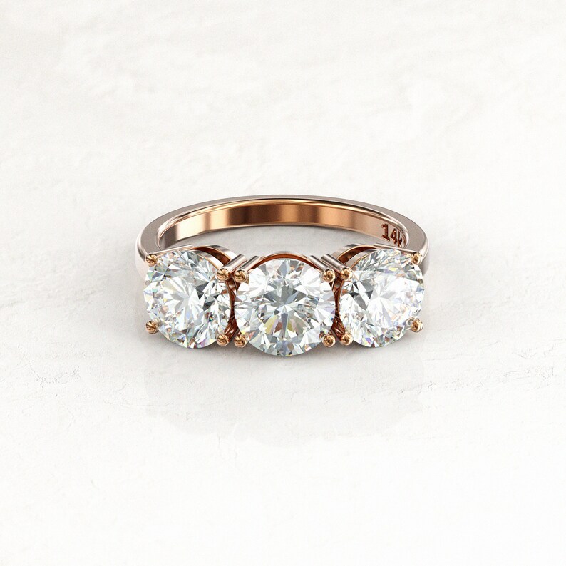 Front view of a two-tone three-stone moissanite engagement ring, with yellow gold prongs and inner settings, a white/silver-colored band, and a visible 14K stamp inside.