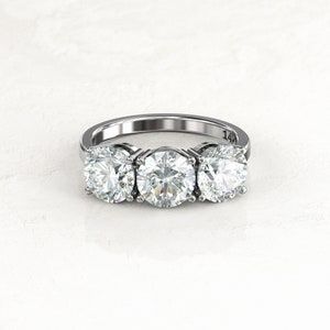 Close front view of three round moissanites in prong settings on a white/silver-colored engagement ring; the inner band is visible behind the stones with a legible 14K stamp.