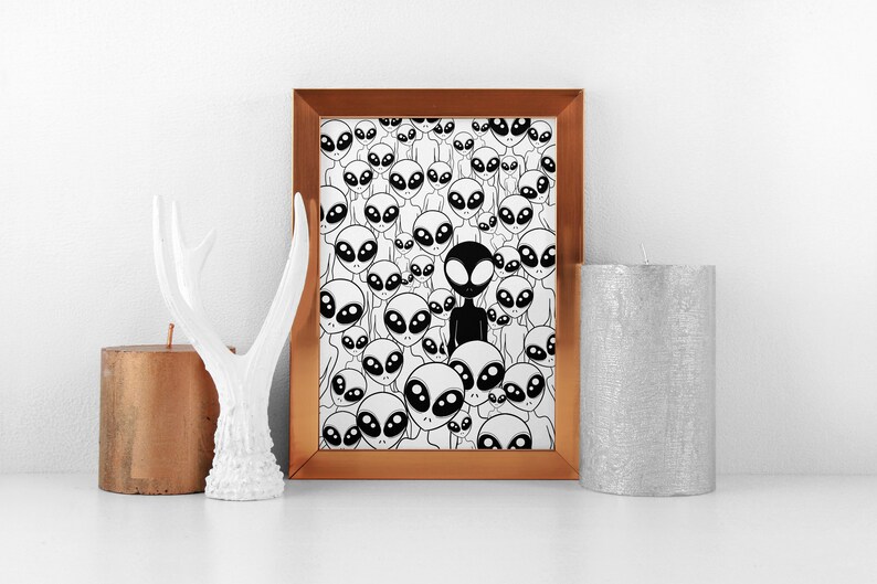 May include: A framed print with a black and white illustration of a crowd of aliens. One alien is black, while the rest are white. The frame is copper colored.