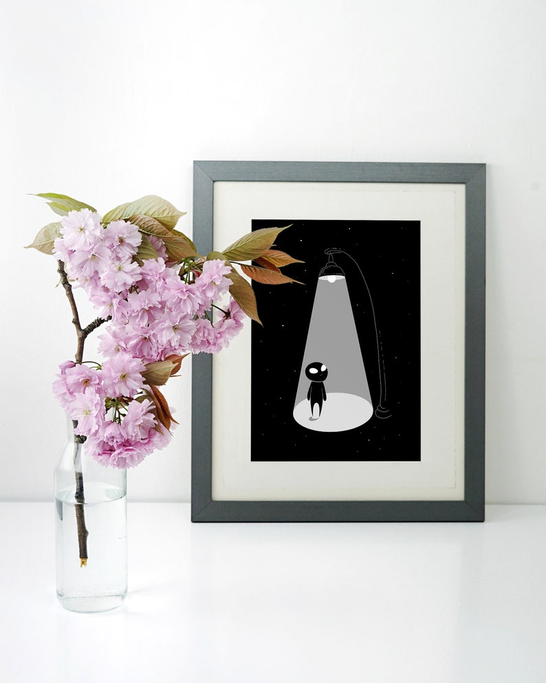 May include: A black and white illustration of a small figure standing in a spotlight. The figure is silhouetted against a black background with white stars. The illustration is framed in a grey frame.