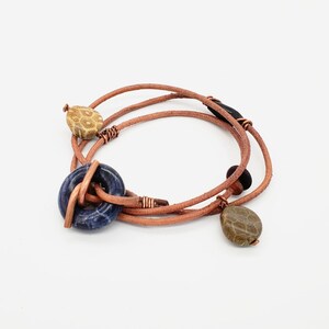 May include: A brown leather bracelet with three different coloured stones. The bracelet is wrapped twice around the wrist and has a copper wire accent.