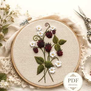 May include: Embroidered artwork showing a bouquet of red berries, white flowers, and green leaves. The design is stitched on a beige fabric within a wooden embroidery hoop. A PDF digital download is available.