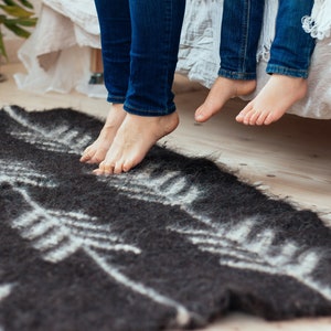 Op de afbeelding: Twee paar blote voeten hangen over de rand van een wit bed, met een zwart-wit gepatroneerd tapijt op de vloer eronder.