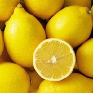 Può includere: Primo piano di diversi limoni giallo brillante, con uno tagliato a metà per rivelare l'interno succoso. I limoni sono raggruppati, mostrando la loro buccia liscia e il colore vibrante.
