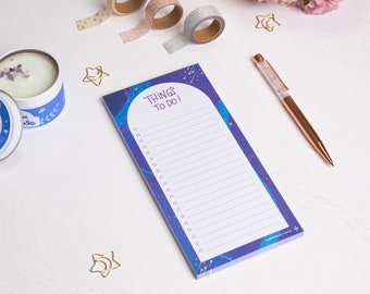 May include: A Things To Do list notepad with a starry night design, featuring the text "THINGS TO DO!" in purple. A rose gold pen, decorative washi tape rolls, and a candle are also visible.