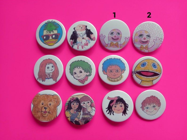 May include: Ten round white buttons with colorful cartoon images. The buttons feature characters from the children's television show, The Wombles. The buttons are arranged in two rows of five. The top row has the numbers 1 and 2 printed above the buttons.