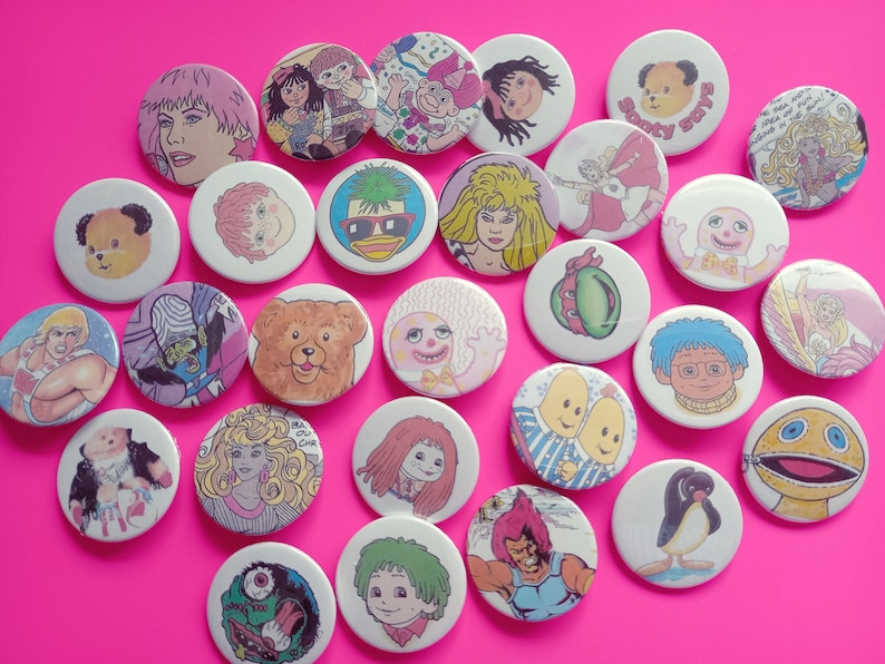 May include: A collection of 25 colorful round pinback buttons featuring various cartoon characters and illustrations. The buttons are approximately 1 inch in diameter and have a white background.