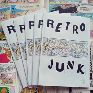 May include: A stack of five white comic books with the title "RETRO JUNK" in large black letters. The number "2" is in green. The comic books are on top of other comic strips and a magazine.