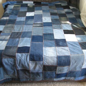 May include: A patchwork quilt made from denim fabric in various shades of blue. The quilt is made up of squares of different sizes and is sewn together with a contrasting thread.