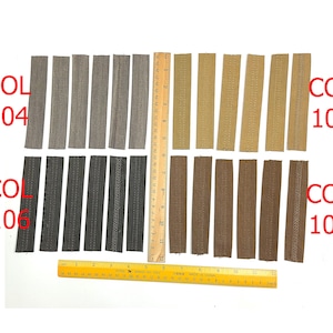 Puede incluir: Una colección de muestras de cremalleras de tela en varios colores, incluyendo gris, beige y marrón, dispuestas sobre una superficie blanca. Se coloca una regla junto a las cremalleras para medir. El texto "COL 104", "COL 105", "COL 106" y "COL 107" es visible.