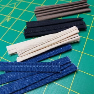 May include: Assortment of fabric trim in various colors and textures, including brown, black, beige, and blue. The trim is arranged on a green cutting mat.