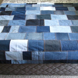 Può includere: Un quilt patchwork realizzato in tessuto denim blu. Il quilt è composto da quadrati di diverse dimensioni e tonalità di blu. Il quilt è steso su un letto.