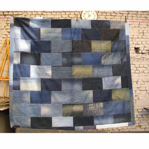 May include: A rectangular quilt constructed from various rectangular patches of denim fabric in multiple shades of blue, ranging from light wash to dark indigo, featuring visible stitching and a patchwork design with a grid-like arrangement.