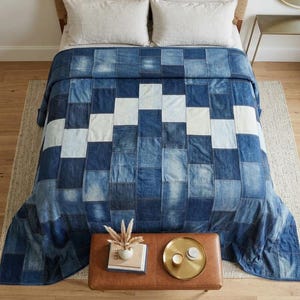May include: A patchwork quilt made from rectangular denim fabric pieces in various shades of blue, ranging from light to dark indigo, arranged in a geometric pattern with a prominent white chevron design running across the center of the blanket.