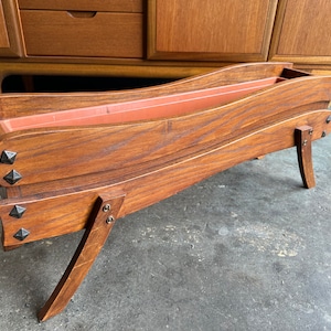 May include: A wooden planter with a curved design and metal accents. The planter is made of dark wood and has a natural finish. It has a rectangular shape and is designed to hold plants.