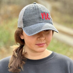 May include: A gray and white baseball cap with a red embroidered "me" on the front. The cap has a mesh back.
