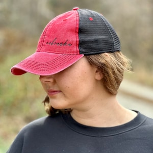 May include: A red and black baseball cap with a mesh back. The front of the cap has the word "remarkable" embroidered in black.
