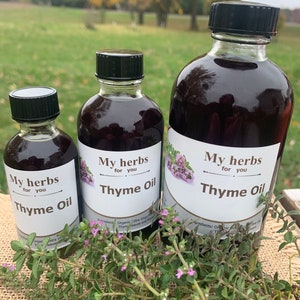 Peut inclure: Trois bouteilles en verre d'huile de thym de différentes tailles. Les bouteilles sont étiquetées "My herbs for you Thyme Oil". Les bouteilles sont posées sur une table avec une brindille de thym devant elles.