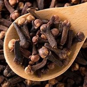 Puede incluir: Primer plano de una cuchara de madera llena de clavos de olor secos. Los clavos de olor son marrones y tienen un ligero tono rojizo.
