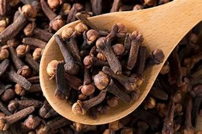 Puede incluir: Primer plano de una cuchara de madera llena de clavos de olor secos. Los clavos de olor son marrones y tienen un ligero tono rojizo.