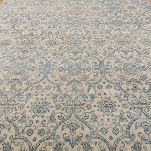 K&ouml;nnte beinhalten: Ein beiger Teppich mit einem komplizierten blauen und wei&szlig;en Blumenmuster. Der Teppich hat einen Used-Look und ist aus einem weichen, pl&uuml;schigen Material gefertigt.