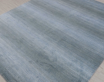May include: A light blue area rug with a subtle ombre effect. The rug has a textured woven surface.