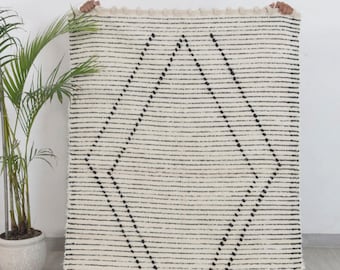 May include: A white and black geometric patterned rug with a fringe border. The rug has a diamond pattern with black dots on a white background.