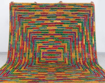 May include: A colorful geometric rug with a repeating pattern of squares and rectangles in shades of red, green, blue, and yellow. The rug has a fringe border.