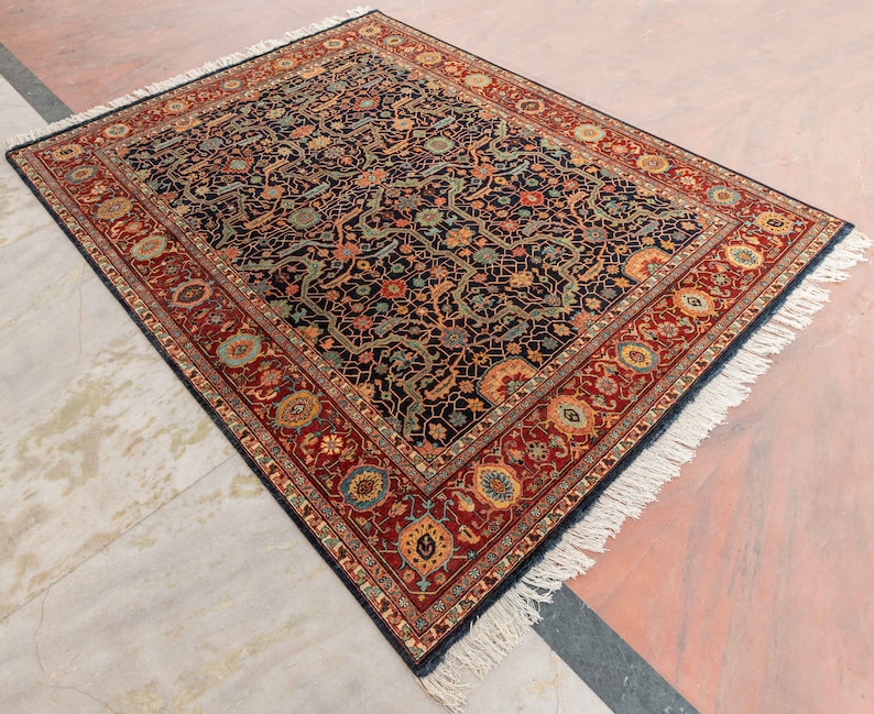 May include: A traditional Persian rug with a dark blue background and intricate floral patterns in shades of red, gold, and green. The rug has a fringed border and is made of wool.