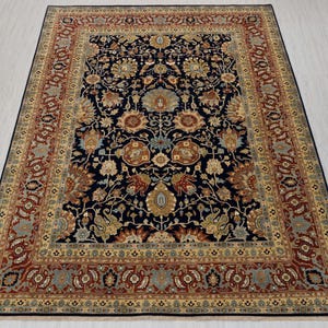 May include: A traditional Persian rug with a dark blue background and intricate floral patterns in shades of red, gold, and cream. The rug has a wide border with a repeating design.