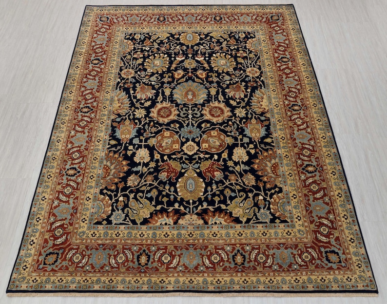 May include: A traditional Persian rug with a dark blue background and intricate floral patterns in shades of red, gold, and cream. The rug has a wide border with a repeating design.