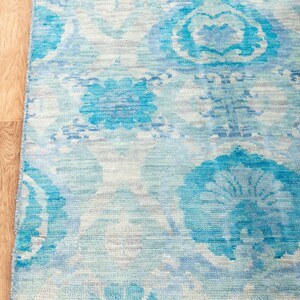 Puede incluir: Una alfombra azul y blanca con un borde de flecos. La alfombra tiene un dise&ntilde;o floral con un aspecto descolorido y vintage.