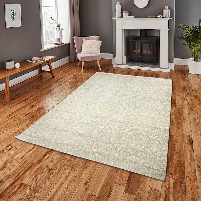 Puede incluir: Una alfombra de color crema con un sutil y complejo patr&oacute;n floral. La alfombra est&aacute; colocada sobre un suelo de madera en un sal&oacute;n.