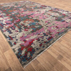 May include: A colorful abstract rug with a gray background and pink, blue, and red accents. The rug has a fringed edge.