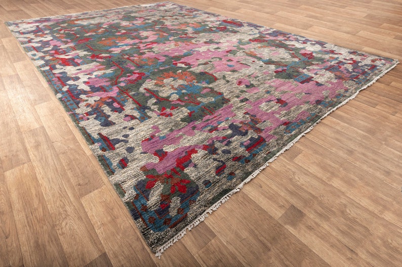 May include: A colorful abstract rug with a gray background and pink, blue, and red accents. The rug has a fringed edge.