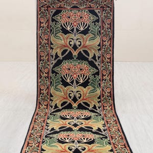 Puede incluir: Una alfombra rectangular con fondo negro y diseño floral. La alfombra presenta patrones y bordes florales rojos, verdes y beige. Una persona sostiene la alfombra.