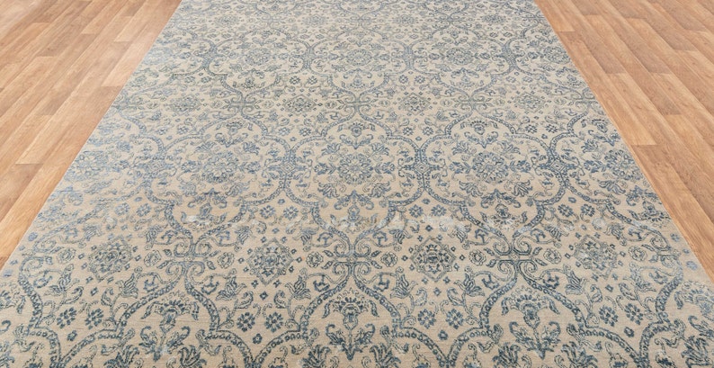 K&ouml;nnte beinhalten: Ein beiger Teppich mit einem komplizierten blauen und wei&szlig;en Blumenmuster. Der Teppich hat einen Used-Look und ist aus einem weichen, pl&uuml;schigen Material gefertigt.