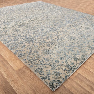 K&ouml;nnte beinhalten: Ein Vintage-Teppich mit cremefarbenem Hintergrund und einem blauen Blumenmuster. Der Teppich hat einen Used-Look und ist perfekt, um jedem Raum einen Hauch von traditionellem Stil zu verleihen.