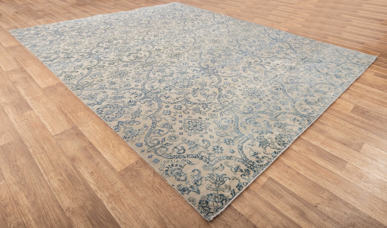 K&ouml;nnte beinhalten: Ein Vintage-Teppich mit cremefarbenem Hintergrund und einem blauen Blumenmuster. Der Teppich hat einen Used-Look und ist perfekt, um jedem Raum einen Hauch von traditionellem Stil zu verleihen.