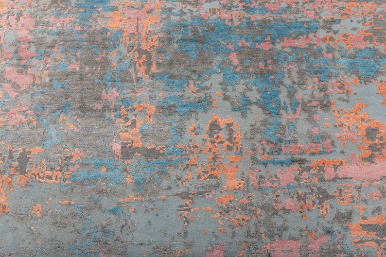 K&ouml;nnte beinhalten: Abstrakter Teppich mit einem Used-Design. Der Teppich hat eine graue Basis mit Akzenten in Blau, Orange und Rosa. Das Design hat ein strukturiertes Aussehen und erzeugt einen modernen Look. Ideal f&uuml;r Wohn- oder Schlafzimmer.