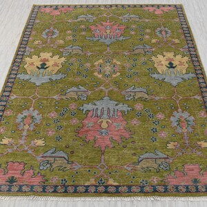 Puede incluir: Una alfombra verde con un patrón floral en tonos de rosa, amarillo y azul. La alfombra tiene un borde azul oscuro con flecos.