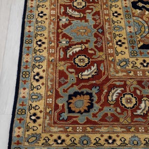 May include: A close-up of a traditional Persian rug with a red, blue, and gold color scheme. The rug has a detailed floral pattern and a fringe border.