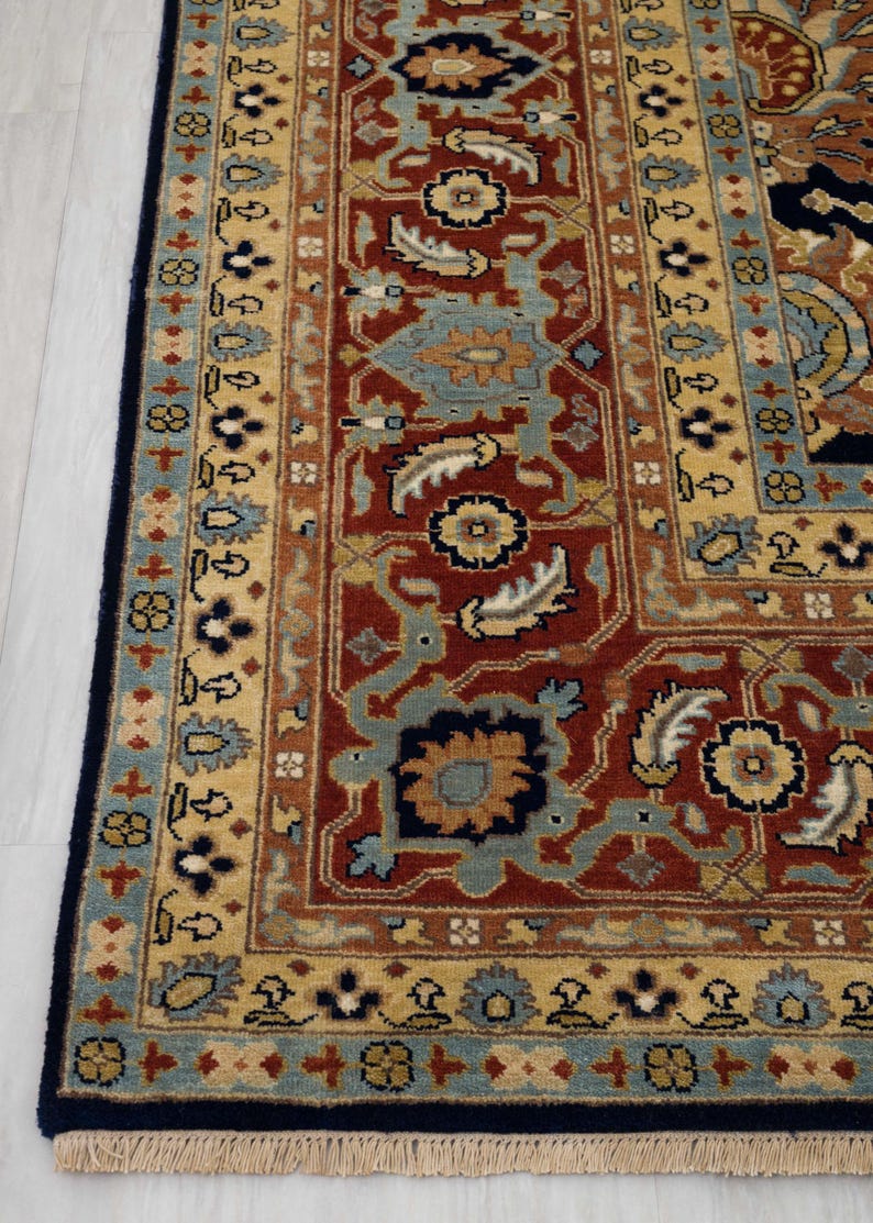 May include: A close-up of a traditional Persian rug with a red, blue, and gold color scheme. The rug has a detailed floral pattern and a fringe border.